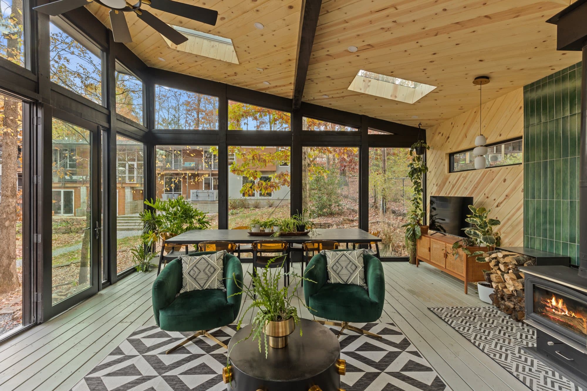 Dining end of the sunroom, with a black table and amber chairs at a full height glass wall facing a neighboring two story house