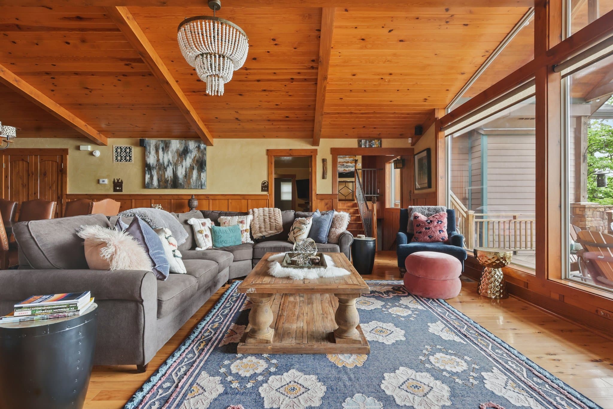 Styled living room with a wood plank ceiling, a sectional sofa and a wall of windows onto the deck in a short term rental cabin in Hot Springs, Arkansas