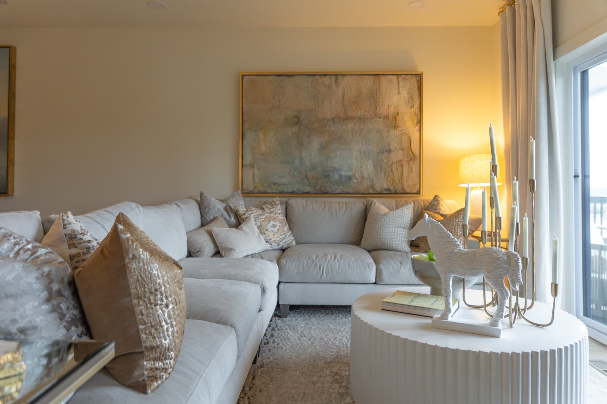 Living room in a short term rental, with a cream sectional under a large gold framed canvas and a round fluted white coffee table