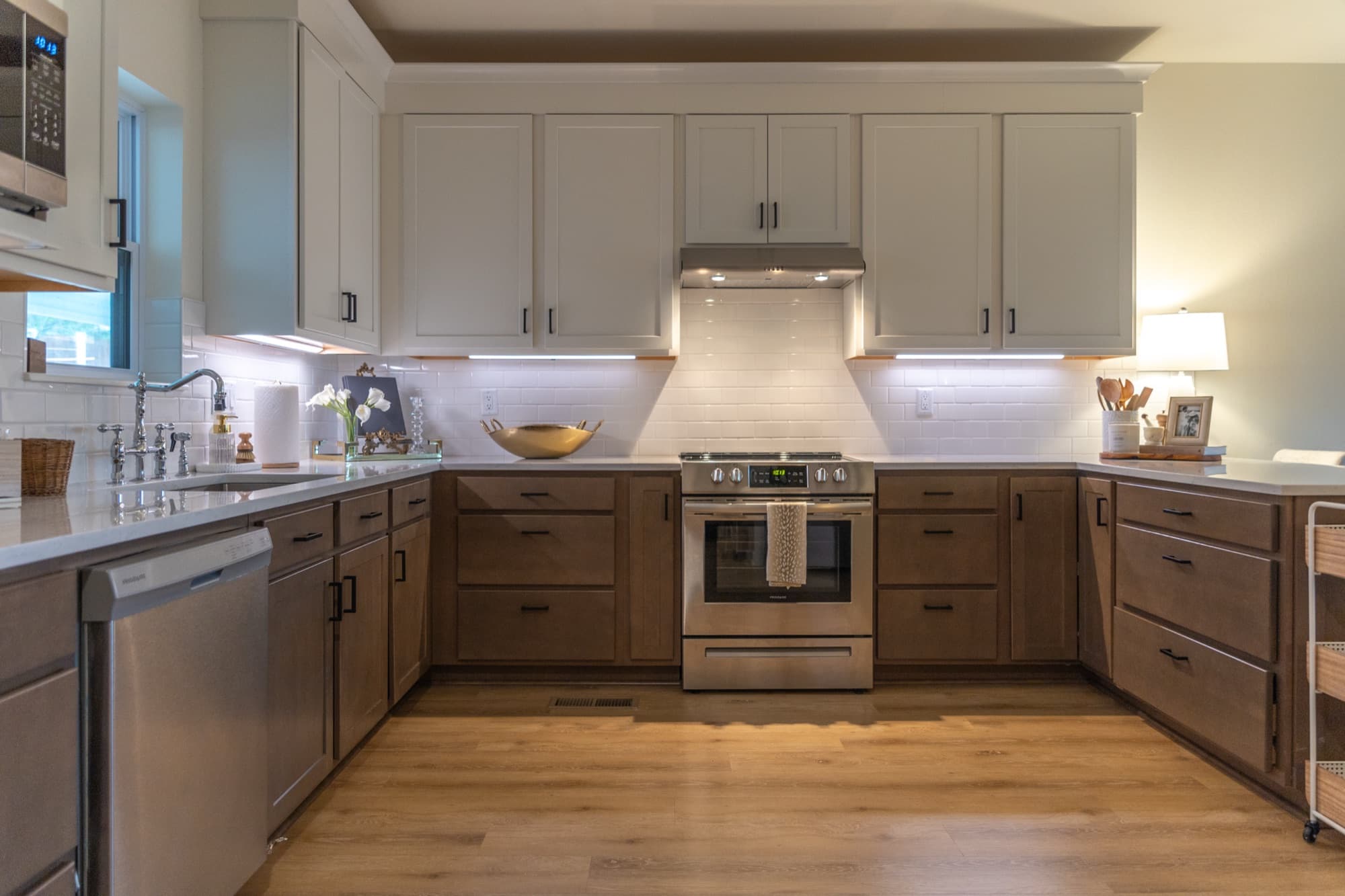 Kitchen in a short term rental, with cream upper cabinets over stained oak lowers, white subway tile, quartz counters and a stainless range