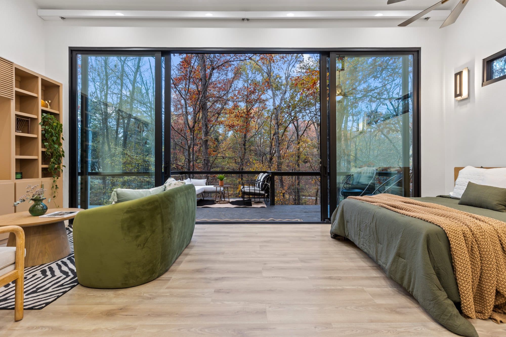 Open plan interior of the stilt cabin rental, with a king bed, a curved olive sofa and sliding doors open onto the deck