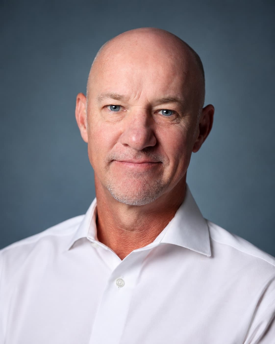 The same man in the same white dress shirt, head and shoulders again, against a cooler slate blue gray backdrop