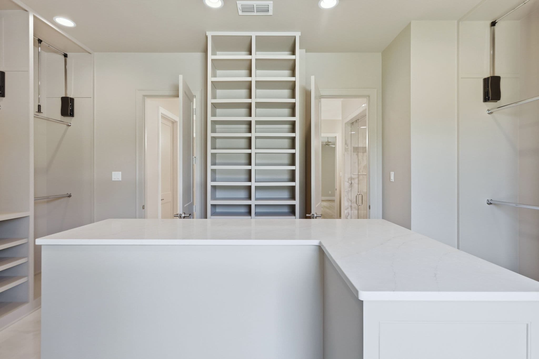 Walk in closet with white built in shelving, hanging rods and a stone topped island in a new construction home in Little Rock, Arkansas