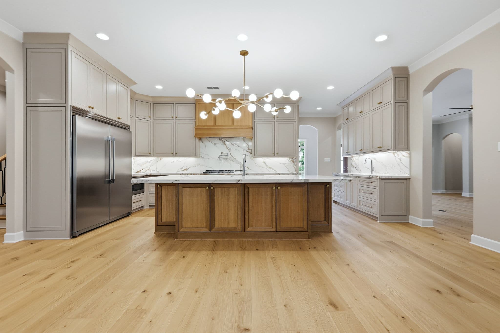 Kitchen with marble counters and backsplash, a wood island and a wood clad range hood in a new construction home in Little Rock, Arkansas