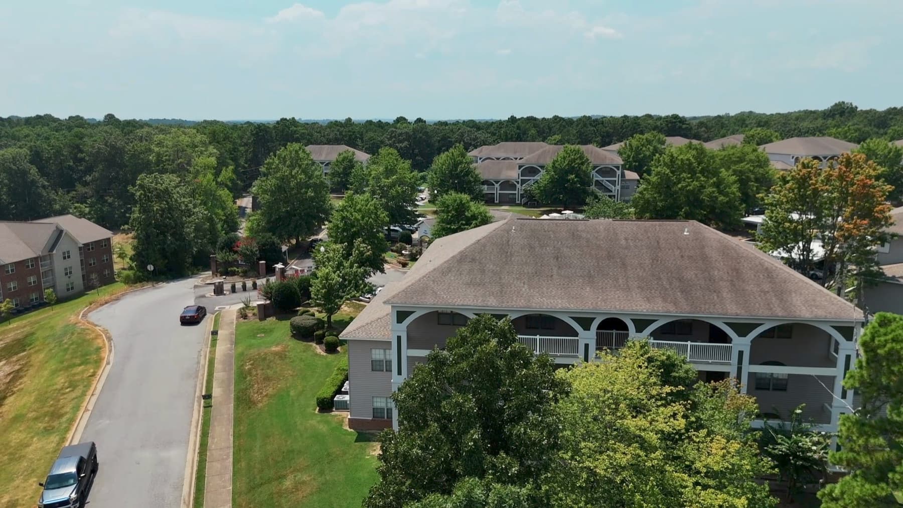 Low aerial of one Arkansas apartment building with white arched breezeways across its face, a curving drive and parked cars at left